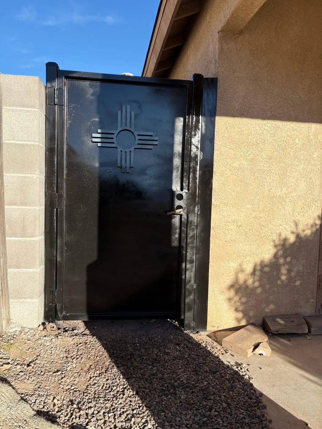 Solid steel side gate with a cut Zia, painted black, beside a stucco house