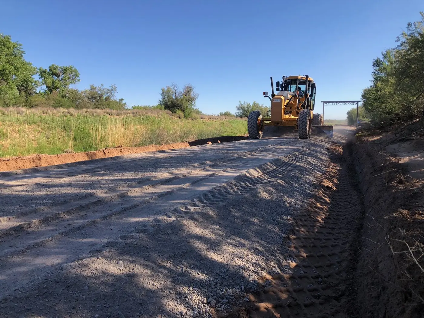 Motor grader spreading base on a ranch road with the entry sign in the distance