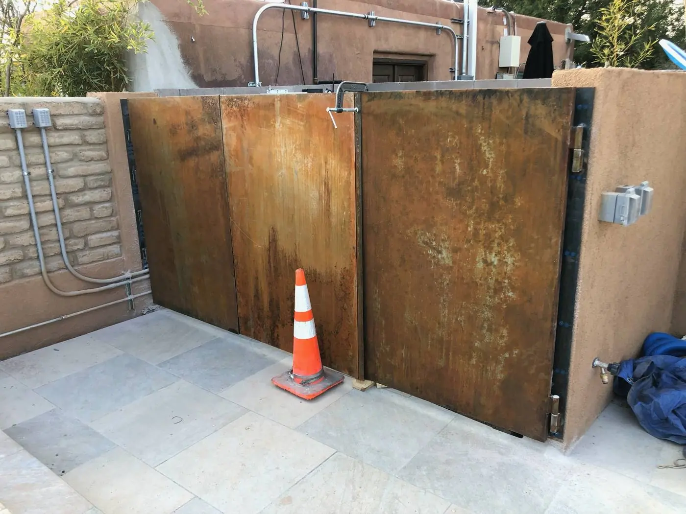 Weathering steel equipment enclosure with a hinged gate between stucco walls